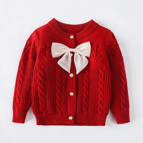 A red cable-knit cardigan sweater for toddlers, featuring a white satin bow accent at the collar and silver button closures, laid flat against a white background.